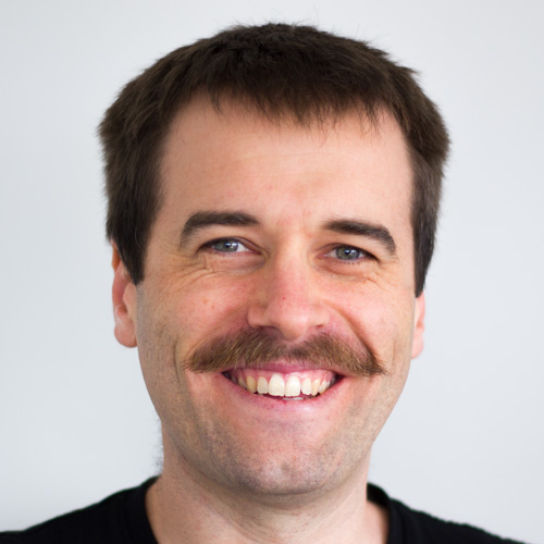 Portrait photo of a smiling man with short hair and a moustache.